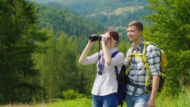 A young couple of tourists admire the beautiful scenery with binoculars. A clear sunny day in the mountains — Stock Video