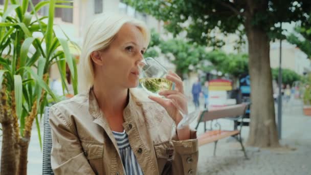 En ung kaukasisk kvinna dricker vitt vin på terrassen på restaurangen. — Stockvideo