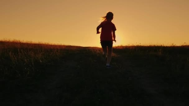 Unbekümmert läuft das Mädchen vor dem Hintergrund des Sonnenuntergangs den Hügel hinauf. Überwindung von Schwierigkeiten, erste Erfolge — Stockvideo