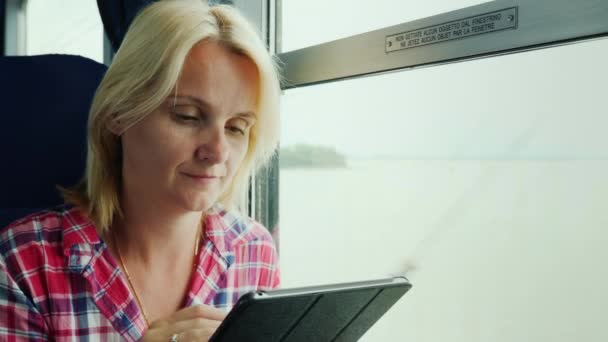 Μια νεαρή γυναίκα που ταξιδεύουν με τρένο. Κάθεται δίπλα στο παράθυρο, χρησιμοποιεί μια ψηφιακή δισκίο — Αρχείο Βίντεο