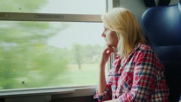 Una giovane donna sta viaggiando su un treno. Guardando fuori dalla finestra — Video Stock