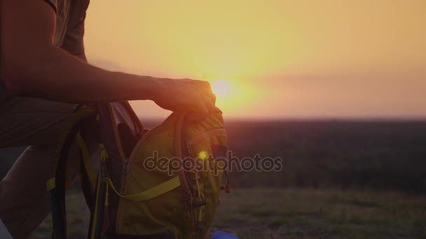 En man packa sin ryggsäck i solnedgången. Förberedelser inför en resa eller vandring — Stockvideo