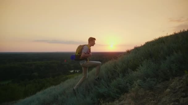 Ten se teenager s batohem leze na horu. Při západu slunce. Aktivní způsob života od mládí — Stock video