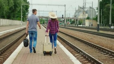 Arkadan görünüş: Genç çift turist ile seyahat çanta mutlu peron Demiryolu boyunca geçinmek. Harika bir yolculuk başlıyor. Steadicam atış