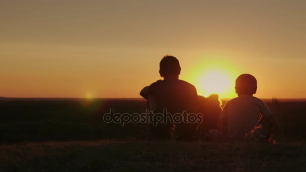Siluetas de dos chicos rurales. Siéntate junto al perro, admirando la hermosa puesta de sol juntos — Vídeo de stock