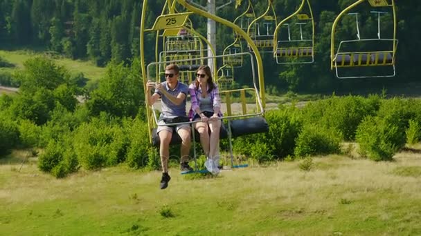 O jovem casal está montado num teleférico. Paisagens fotográficas. Férias nas montanhas no verão — Vídeo de Stock