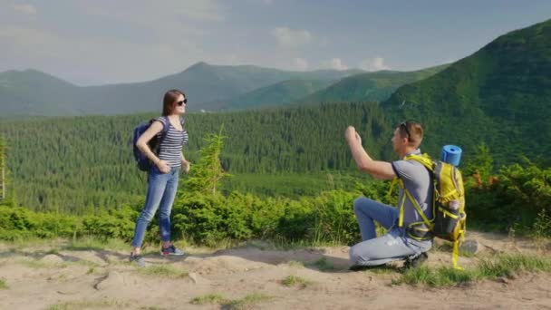 Una joven pareja es fotografiada en un pintoresco mset en el fondo de las montañas cubiertas de bosque. El tipo toma fotos de su novia — Vídeos de Stock