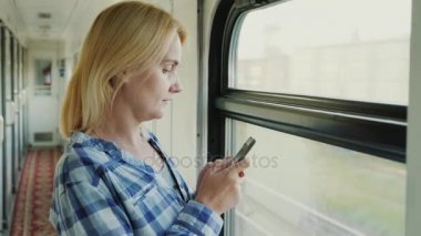 Genç beyaz bir kadın tarafından tren vagonuna penceresinde duruyor. Bir akıllı telefon kullanır. Her zaman online