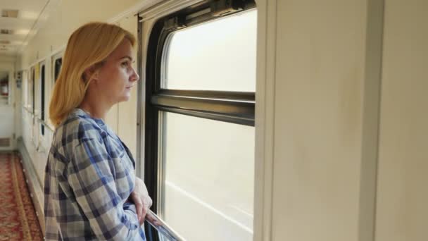 Egy fiatal nő úgy néz ki, a vonat ablakon. -A ' a folyosón, a vonat van mozgó böjt. Álmok és utazások — Stock videók