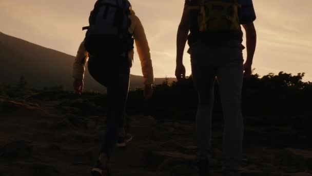 Couple with backpacks behind their back hitting each other in the rays of the setting sun. Success on top and leadership — Stock Video