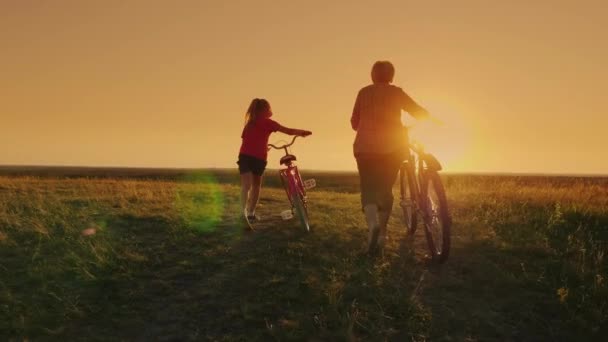 Communication des générations. Grand-mère et petite-fille vont ensemble au coucher du soleil, conduisent des vélos . — Video
