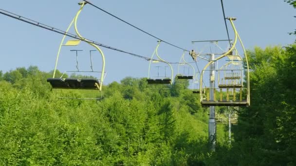 Säten av skidliften. De rör sig uppåt mot bakgrund av en skog som täckt med en skog. Semester i bergen i sommar — Stockvideo