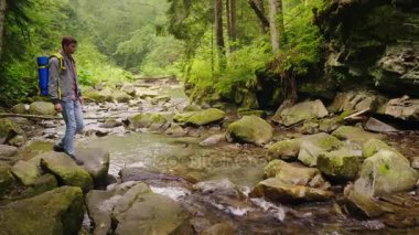 Genç bir erkek turist ormandaki bir dağ nehir geçiyor.
