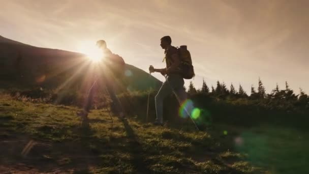 Twee reizigers klimt een berg. Silhouetten in de stralen van de ondergaande zon. — Stockvideo