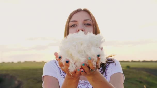 A young woman is playing with a gentle light down. Blows on a pile of feathers, they fly in all directions. — Stock Video