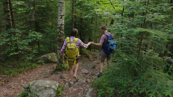 観光客のカップルは、絵のように美しい山の道に沿って歩きます。日没前に太陽が美しく輝いている。冒険と生活のアクティブな方法 — ストック写真