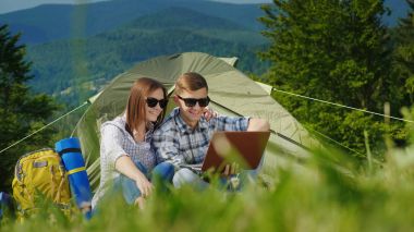 İki turist kamp içinde dizüstü bilgisayarlar kullanıyorsunuz. Pitoresk dağlar arka planı