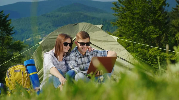 İki turist kamp içinde dizüstü bilgisayarlar kullanıyorsunuz. Pitoresk dağlar arka planı