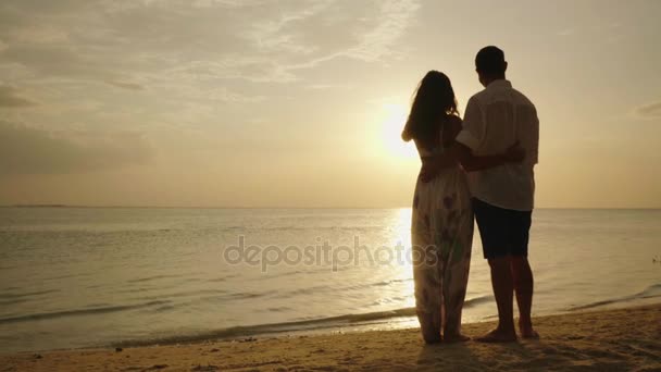 Egy fiatal pár állandó a strandon megcsodálta a naplemente, a tenger felett