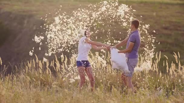 Pillow fight. Young couple are madly having fun. A woman is beating her pillow with a friend