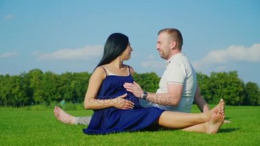 Onun hamile eşi parkta yeşil çim üzerinde rahatlatıcı genç kocasıyla