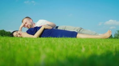 Bir adam hamile eşi olan yeşil çim üzerinde yalan söylüyor. Mavi gökyüzü arka planı