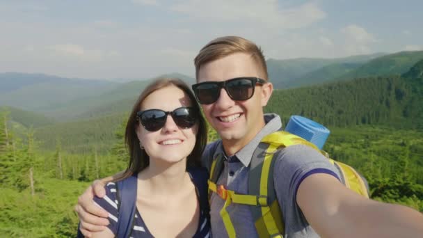 Un par de turistas se fotografiaron, sonriendo a la cámara. En el contexto de un pintoresco paisaje de montaña — Vídeos de Stock