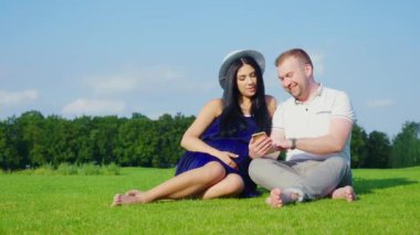 Genç çift beklentisiyle bir çocuk. Birlikte parkta tutun, bir akıllı telefon kullanır