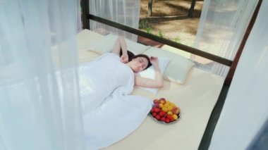 Genç kadının bir tabak meyve perdeler, yanında kaplı bir tembel olarak uyanır. Güzel romantik tatil. Yatakta kahvaltı