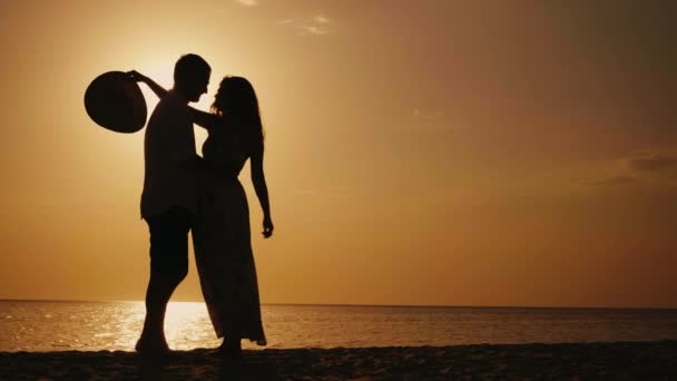 热恋中的情侣的轮廓。他们互相看看，拥抱和亲吻日落时分。背景下的大海或海洋 — 图库视频影像