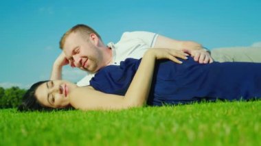 Hamile eşi olan koca yeşil çim üzerinde yalan söylüyor. Mavi gökyüzü arka planı