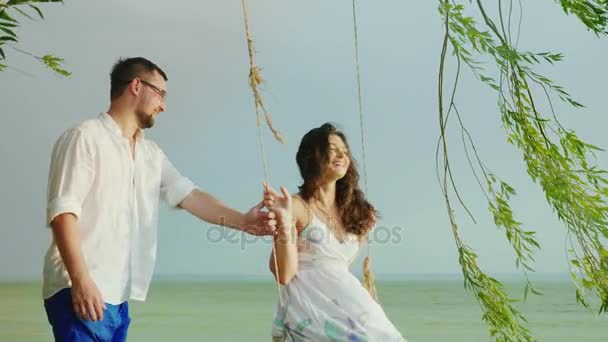 Pessoas felizes à chuva. Um homem está montando sua namorada em um balanço, são felizes juntos — Vídeo de Stock