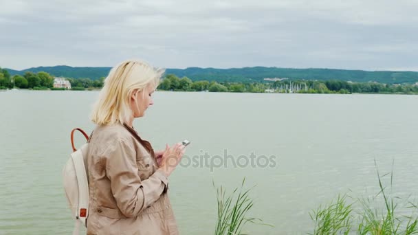 Vrouw loopt rond het meer, met behulp van een mobiele telefoon. Het Balatonmeer in Hongarije. Steadicam schot — Stockvideo