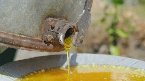 Fresh unfiltered honey flows out of the honey machine. The hand opens the crane. Side view