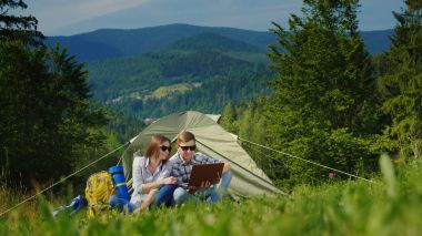 Bir kaç turist kamp içinde dizüstü bilgisayarlar kullanarak. Pitoresk dağlar arka planı