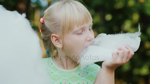 クールな金髪女の子 6 歳は、公園で甘い綿を食べています。フィールドの浅い深さを持つ肖像画 — ストック動画