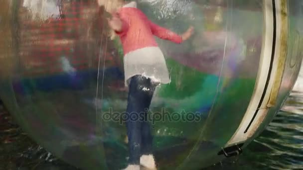 La fille essaie de couler sur ses pieds et de garder l'équilibre à l'intérieur de la boule transparente qui flotte sur l'eau dans la piscine — Video