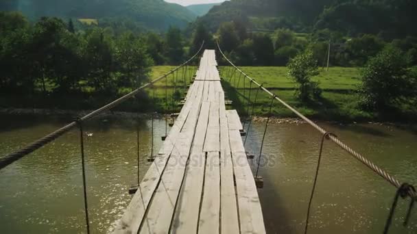 POV steadicam shot: Puente de cuerda de tensión con cubierta de madera sobre el arroyo de la montaña. Vídeo de 4K 10 bits — Vídeo de stock