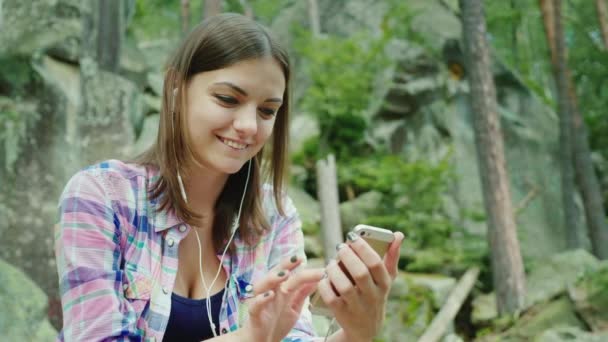 A young woman tourist uses a smartphone in a hike. Sits resting against the rocks in the mountains — Stock Video