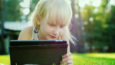 Sarışın kız 6 yıl tablet üzerinde oynayan duygusal tepki verir. Evin arka bahçesinde çim üzerinde yalan