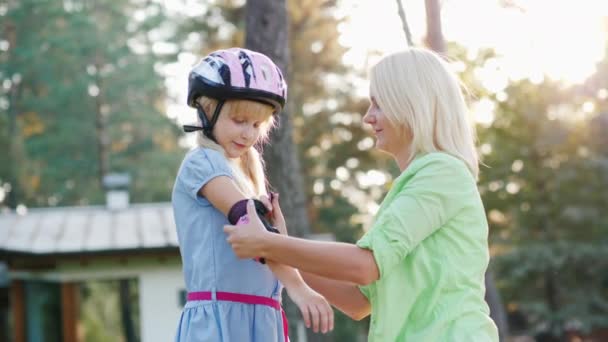 Tiro em câmera lenta: Mãe vestidos filhas de cotovelos para andar de bicicleta ou patins. Cuidados dos pais — Vídeo de Stock