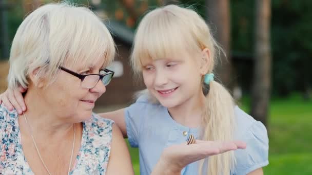 Mormor med hennes barnbarn tittar på en liten snigel i handen. Koncept - naturen och livet runt, aktiva äldre — Stockvideo