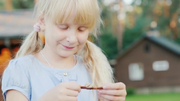 A 6-year-old girl looks at a small snail in her hands. Concept - communication with nature, life around us — Stock Video