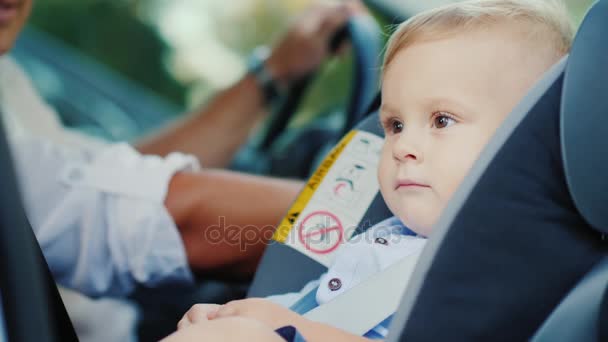 Un niño pequeño está sentado en un asiento de coche cerca de su padre, sonriendo felizmente. Concepto - seguridad y cuidado — Vídeos de Stock