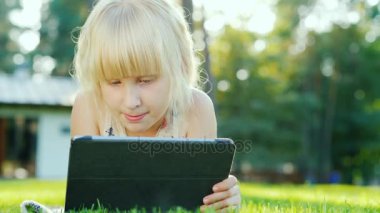 Sarışın kız bir tablet kullanır. Evin arka bahçesinde çim üzerinde yalan
