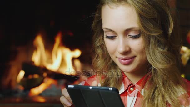 Portret van een aantrekkelijke vrouw: die werkt met de Tablet PC. Is verlichte open haard op de achtergrond. Concept: gezelligheid en technologie — Stockvideo