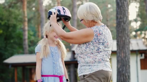 La mujer mayor lleva un casco protector para su hija de 6 años. El cuidado y la protección del concepto de los padres — Vídeos de Stock