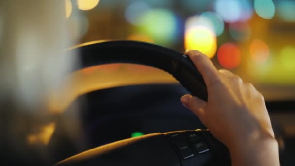 Ženské ruce na volant auta. Jízdy přes noční město, krásný bokeh z protijedoucí auta — Stock video