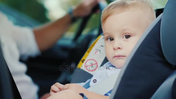 Retrato de un niño lindo, sentado en un asiento de coche para niños cerca del Papa. Concepto de seguridad y cuidado infantil — Vídeos de Stock