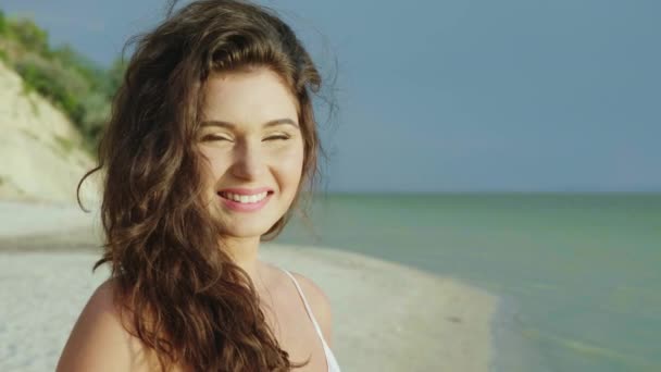Портрет молодої жінки з довгим волоссям на пляжі. Посміхаючись, дивлячись на камеру — стокове відео